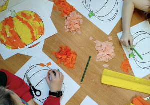 Dzieci pracują nad jesiennymi dyniami.