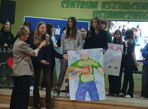 Uczniowie prezentują przygotowany przez siebie plakat. Znajdują się na scenie.